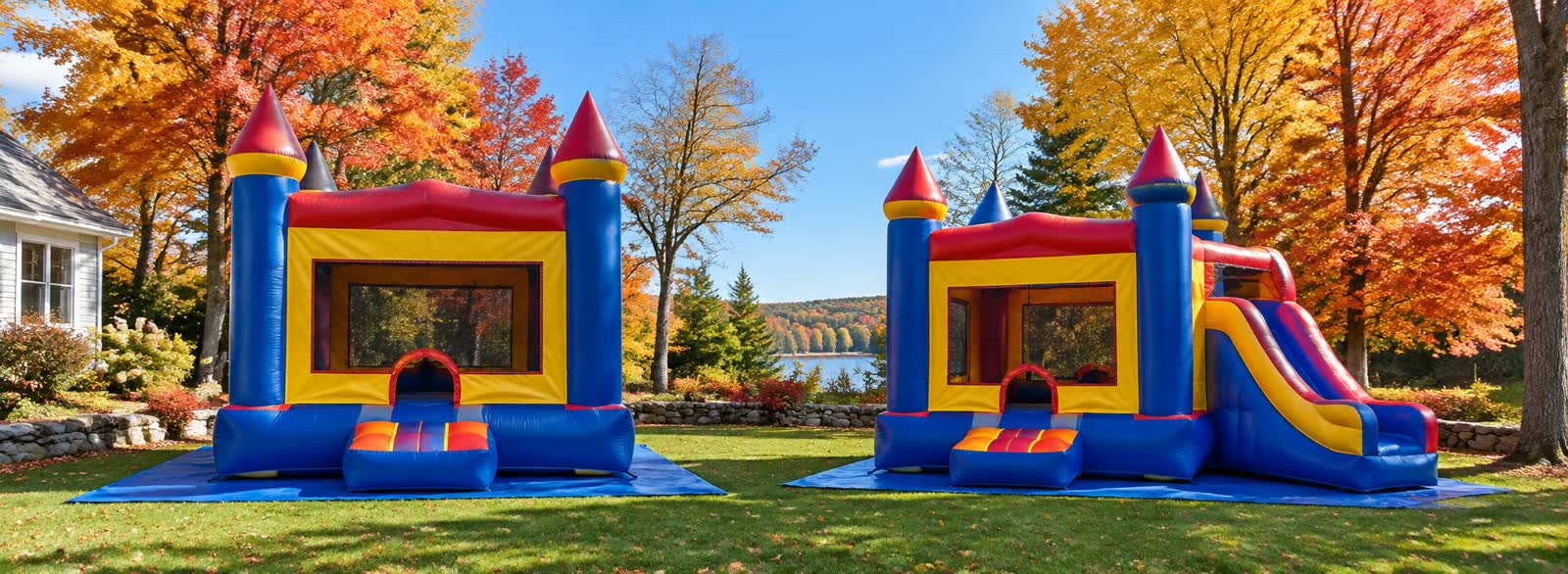 Two bounce house castles set up on a lawn surrounded by bright fall foliage